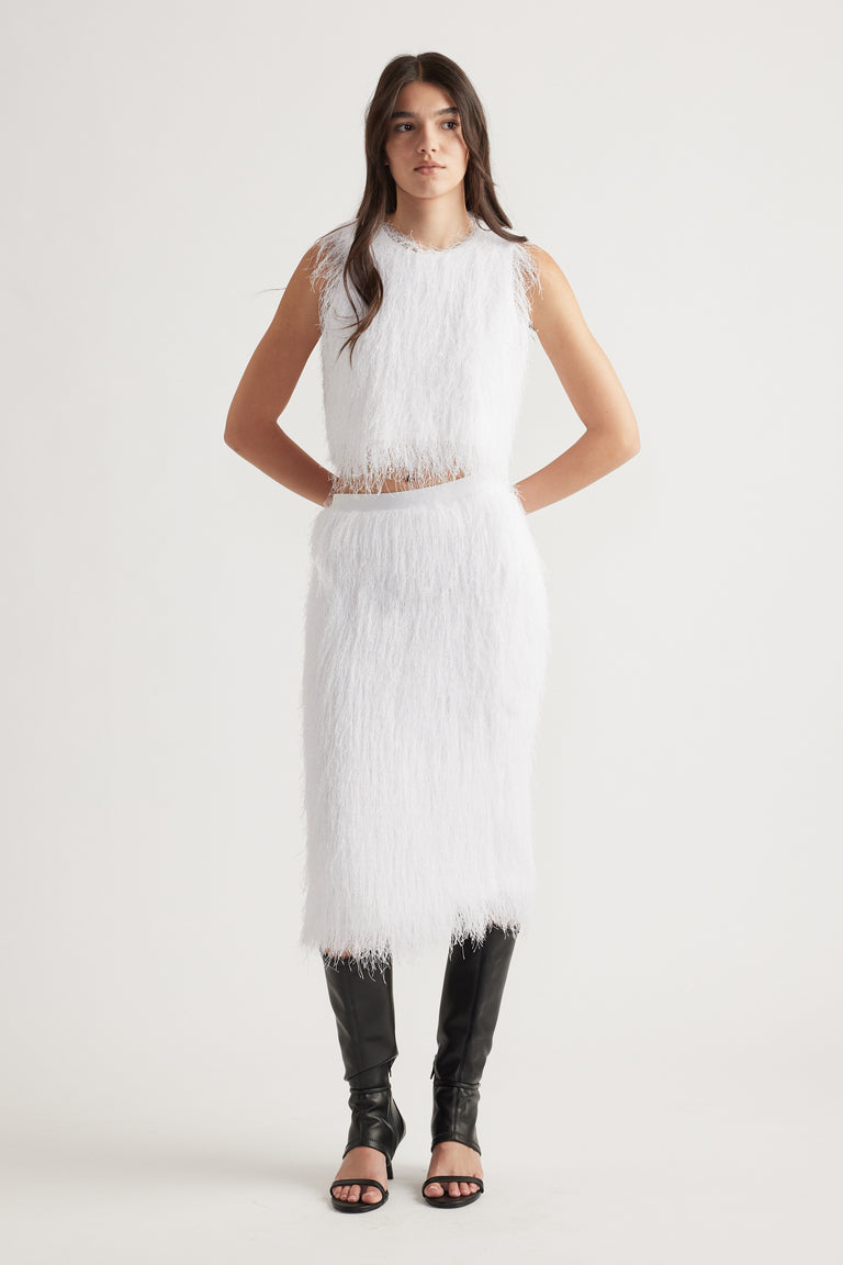 Woman wearing a white textured sleeveless top with matching midi skirt paired with black knee-high heeled boots
