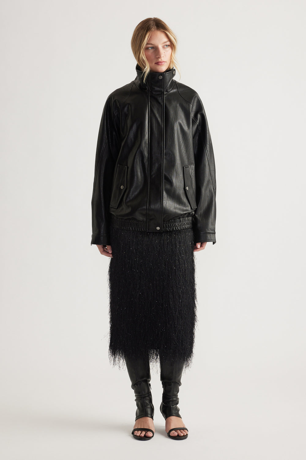 Woman wearing a black fringed midi skirt paired with a loose black leather jacket and open-toe heels