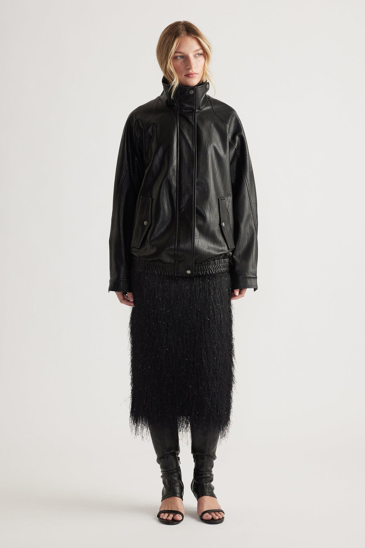 Woman wearing a black fringed midi skirt paired with a loose black leather jacket and open-toe heels