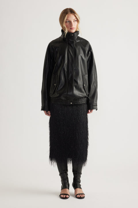 Woman wearing a black fringed midi skirt paired with a loose black leather jacket and open-toe heels