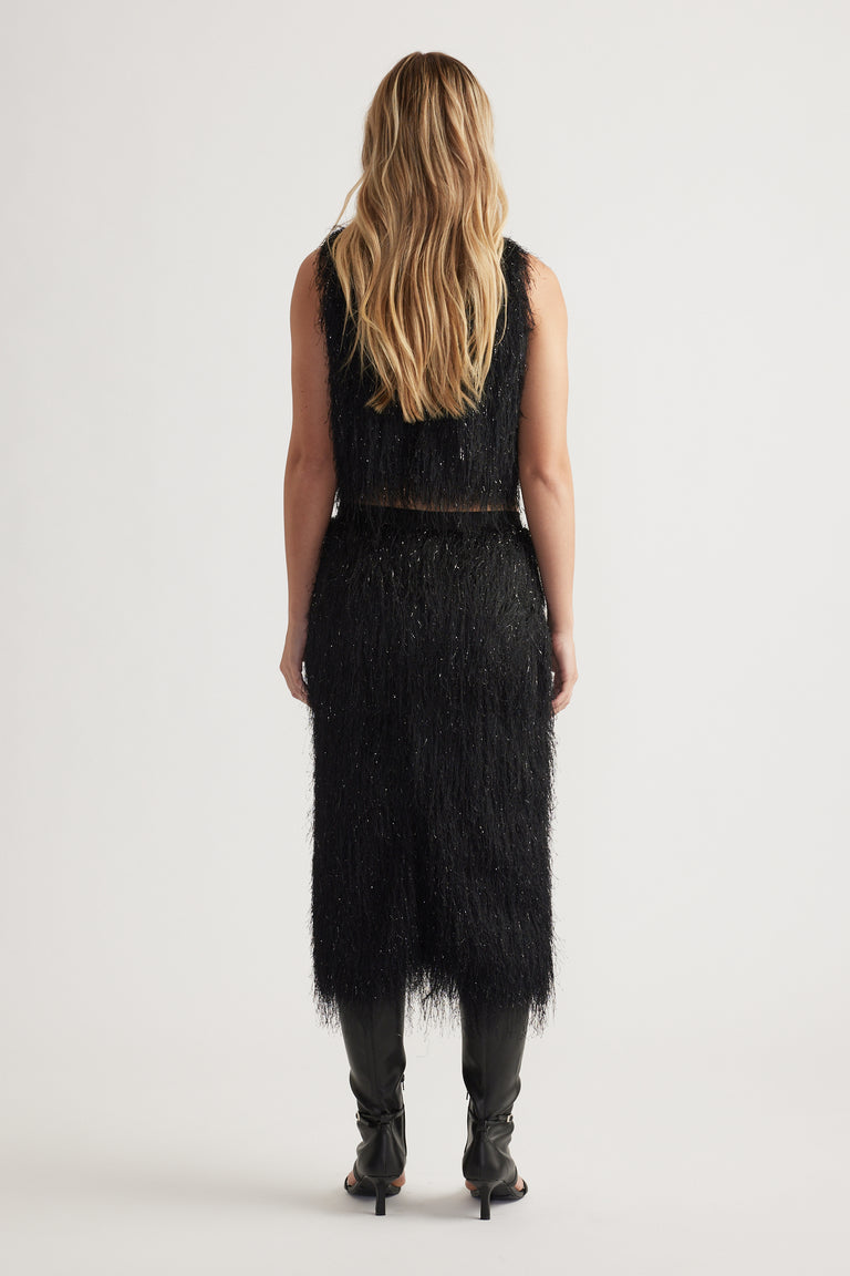 Woman seen from behind wearing a black fringed midi skirt and matching sleeveless top with black heeled boots