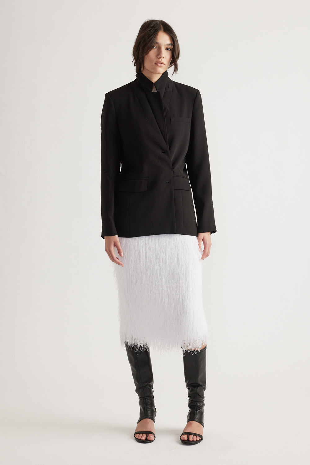 Woman wearing a tailored black blazer paired with a textured white midi skirt and black open-toe tall boots.