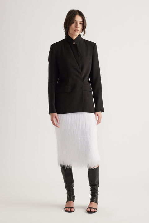 Woman wearing a tailored black blazer paired with a textured white midi skirt and black open-toe tall boots.