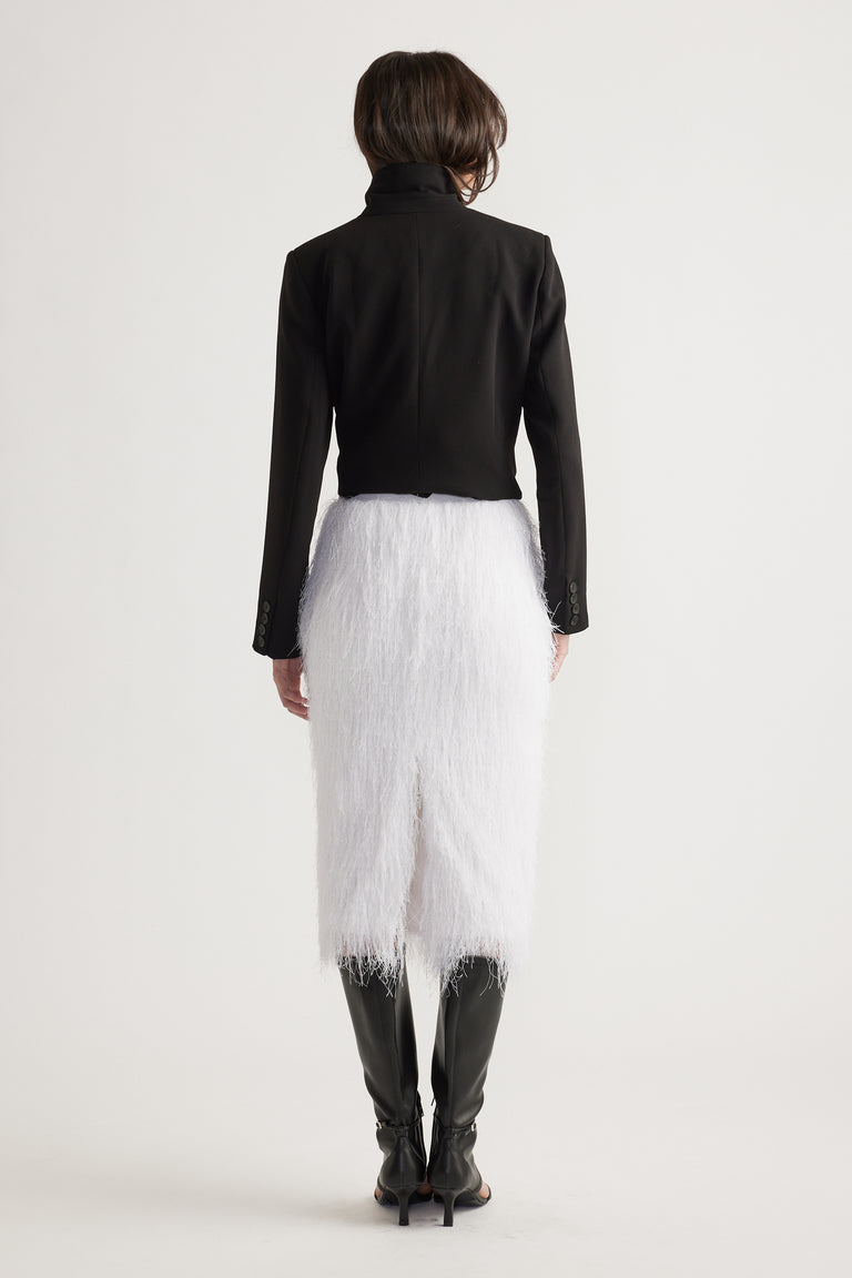 Woman wearing a white fringed midi skirt paired with a fitted black blazer and tall black boots from behind.