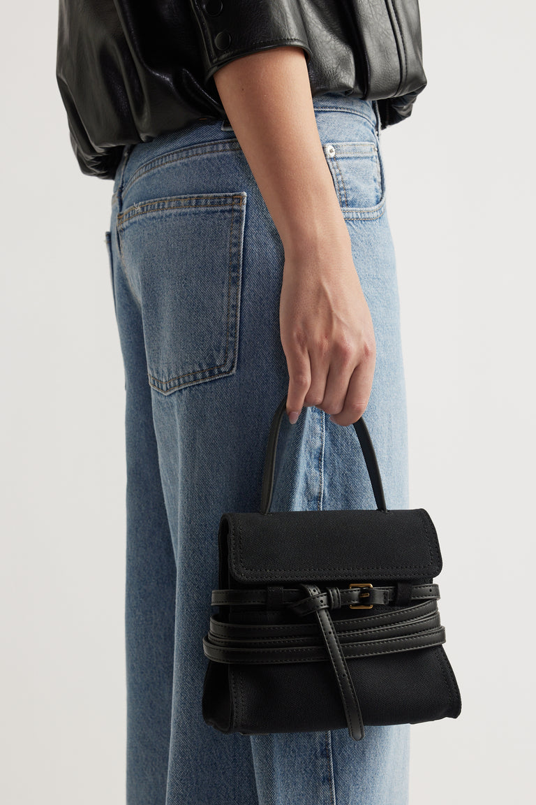 Woman holding a black structured handbag with buckle detail paired with light blue high-waisted jeans and a black top