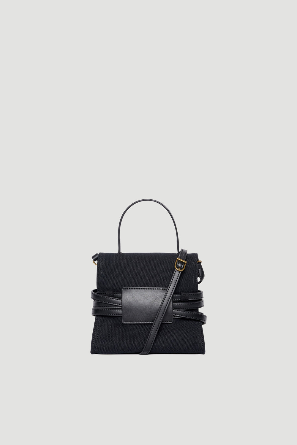 Black cotton bag with leather buckle detail, top handle, and adjustable crossbody strap against light background