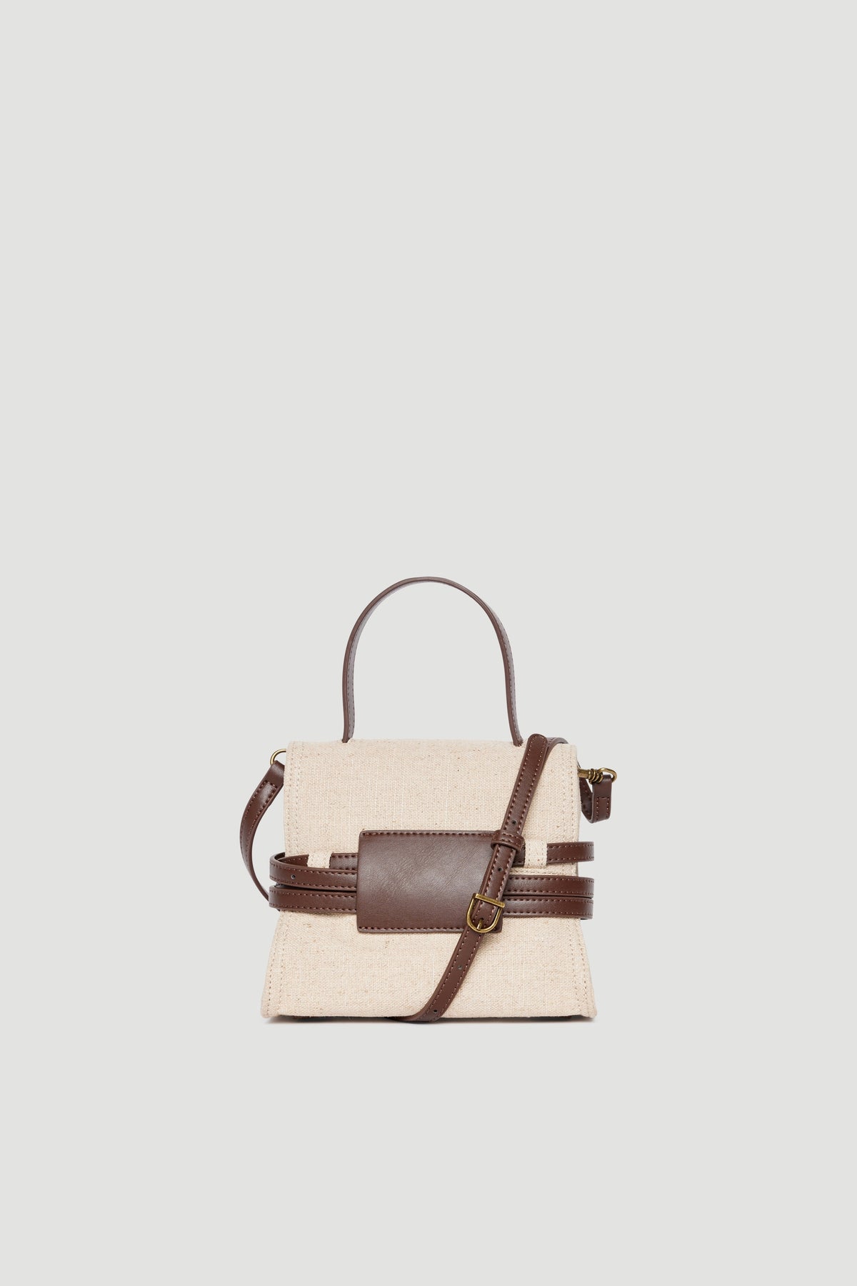 Small structured handbag in natural cotton with dark brown leather strap and buckle detail against plain background
