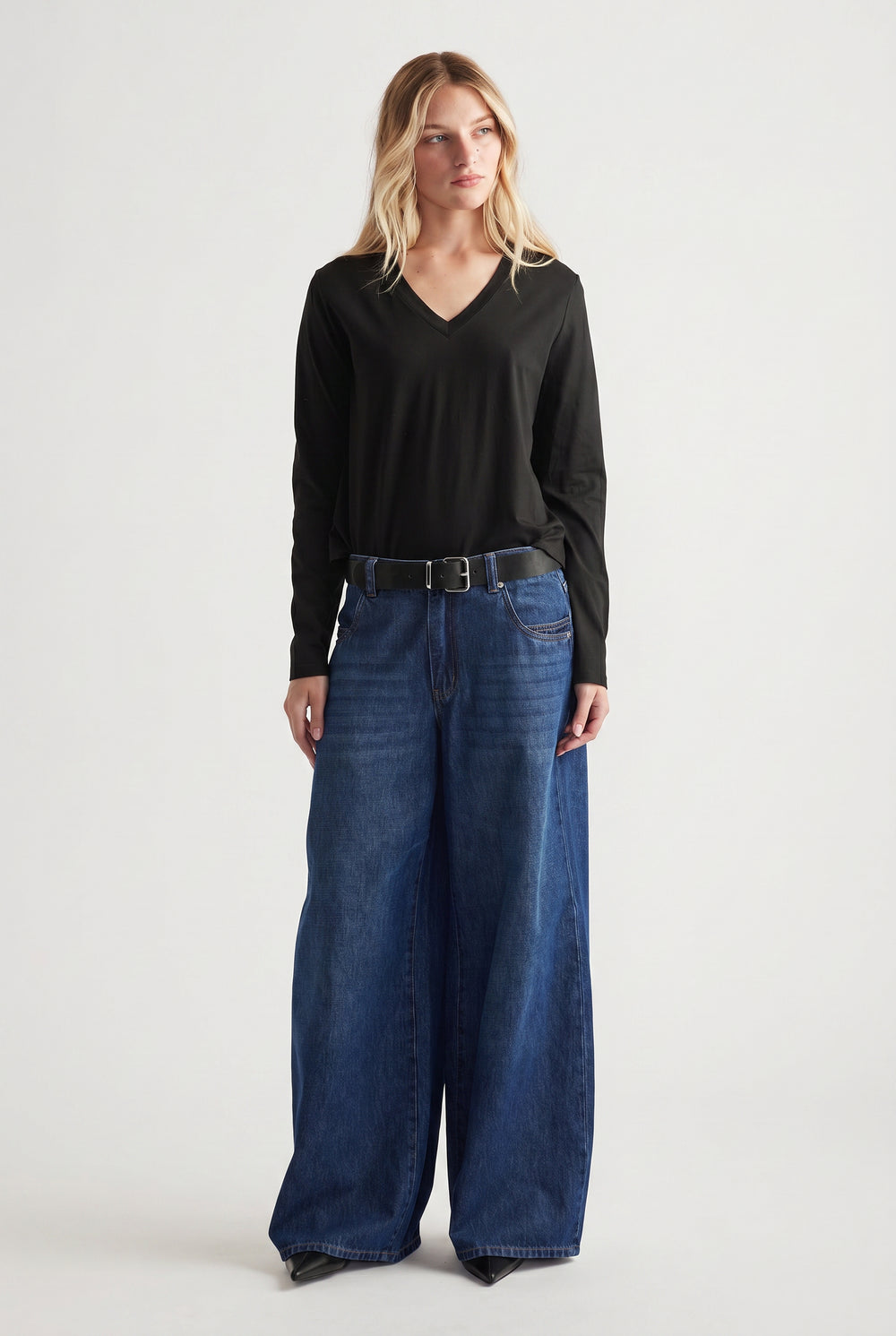 Woman wearing a black V-neck long sleeve top tucked into wide-leg dark blue jeans with a black belt.