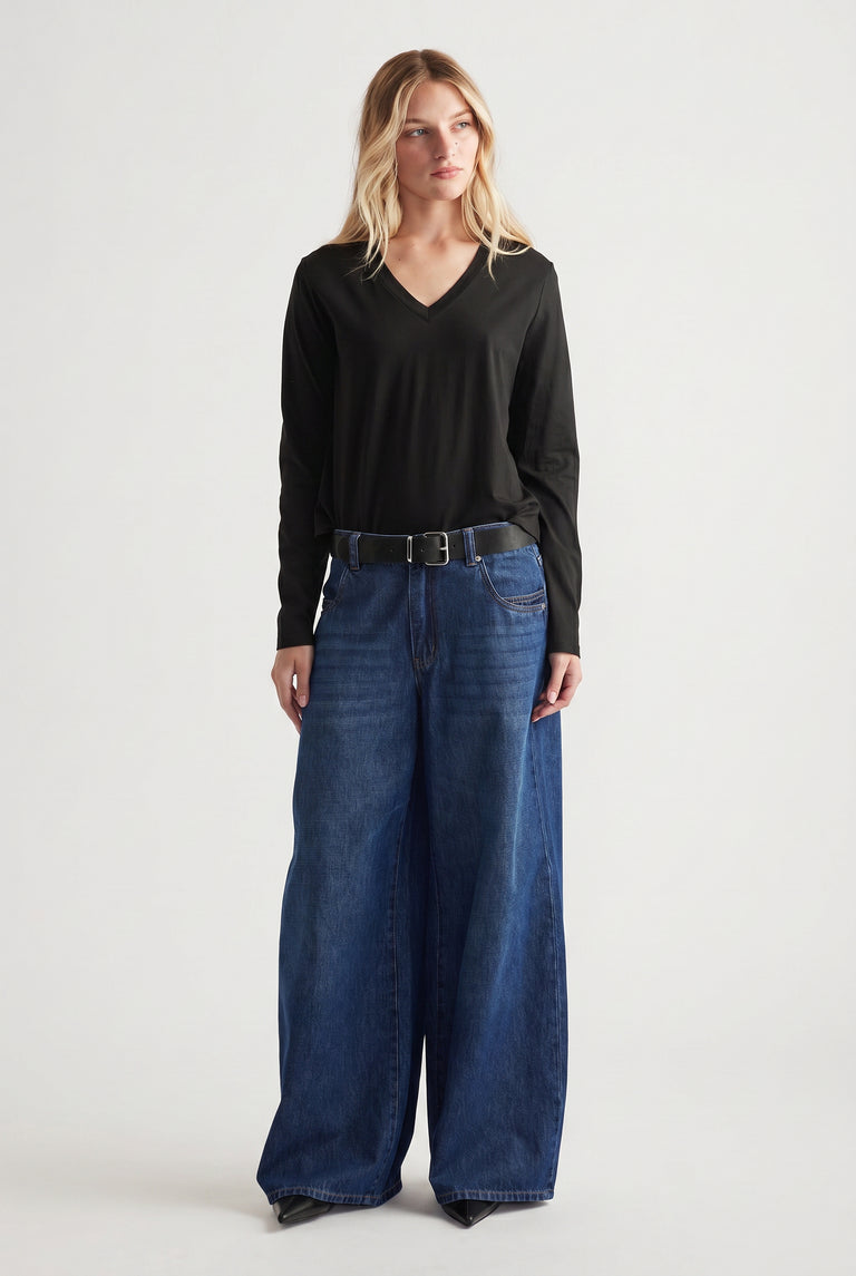 Woman wearing a black V-neck long sleeve top tucked into wide-leg dark blue jeans with a black belt.