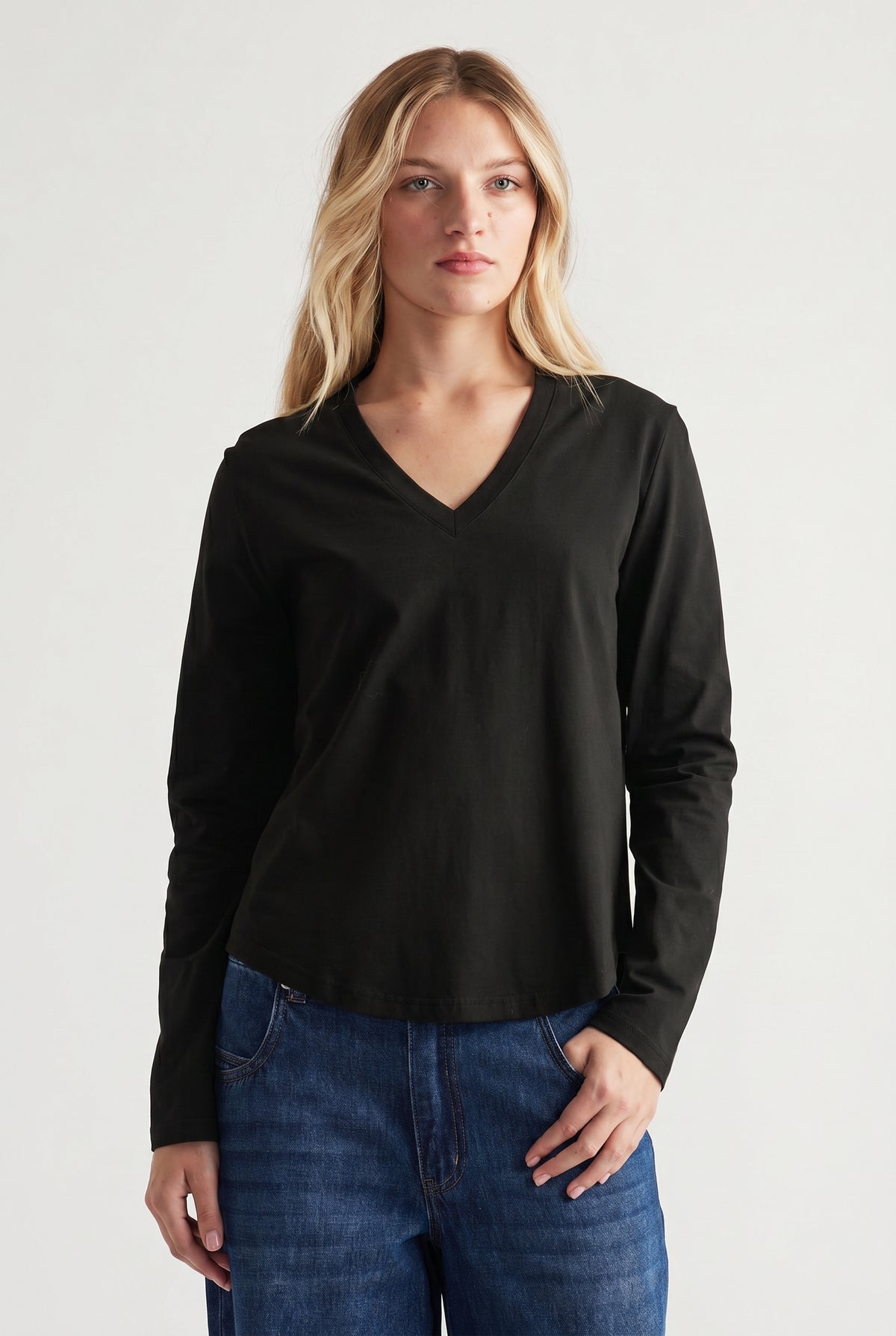 Woman wearing a black V-neck long sleeve top paired with relaxed blue jeans in a minimal studio setting