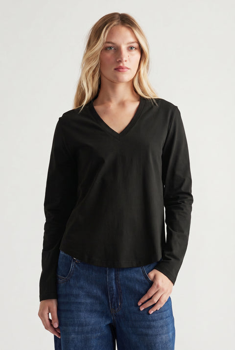 Woman wearing a black V-neck long sleeve top paired with relaxed blue jeans in a minimal studio setting