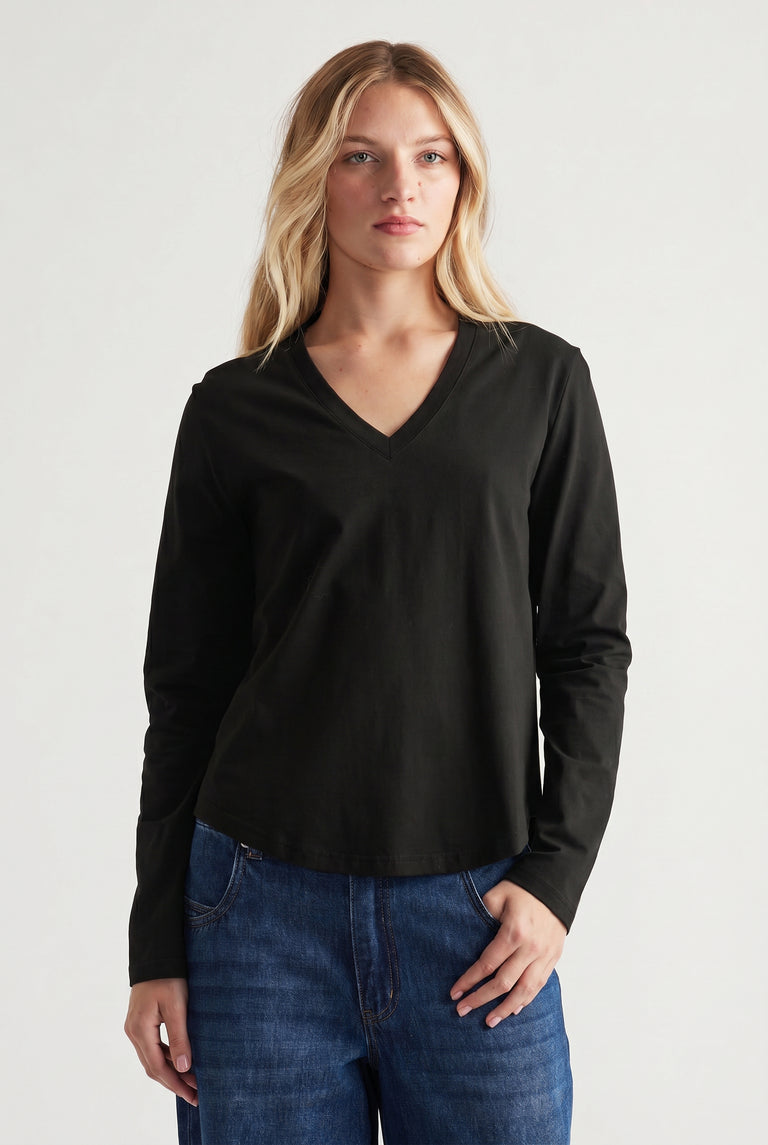 Woman wearing a black V-neck long sleeve top paired with relaxed blue jeans in a minimal studio setting