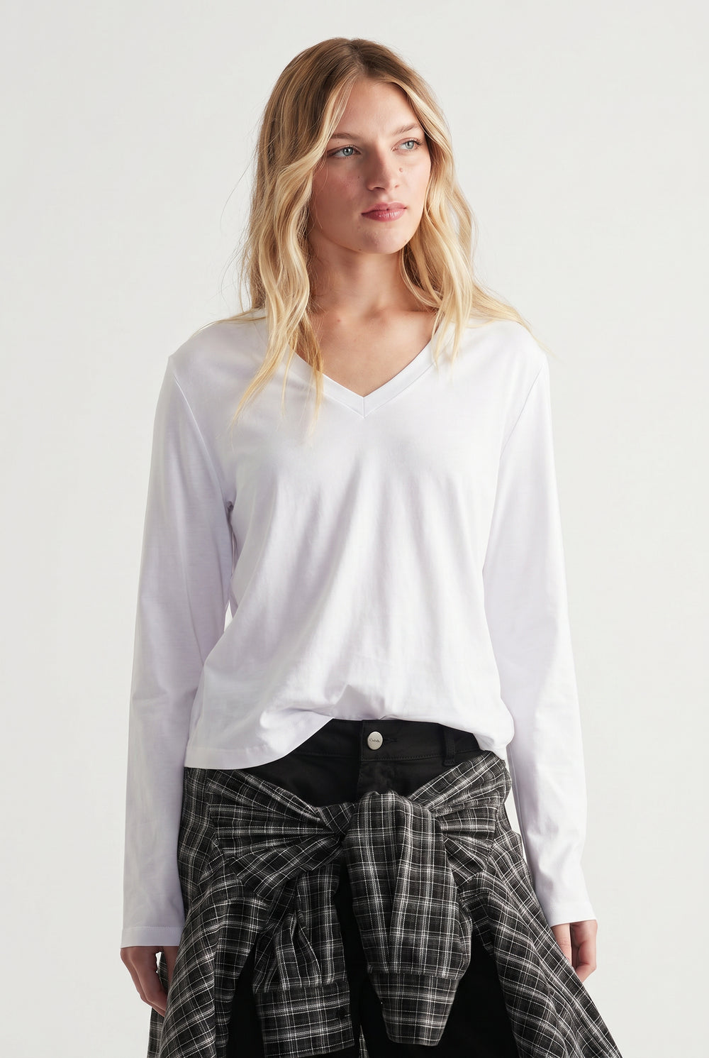 Woman wearing a white V-neck long sleeve top with a black plaid shirt tied around waist for casual style