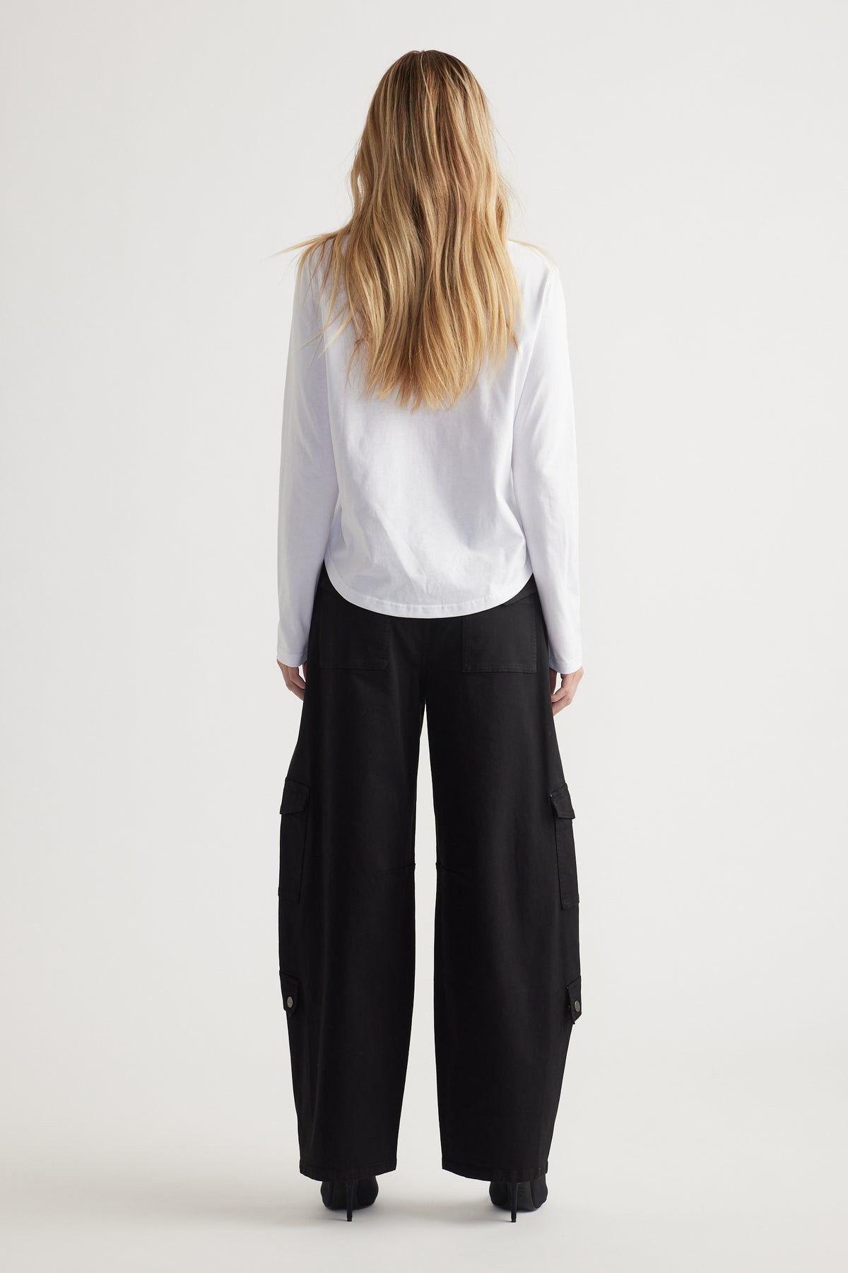 Woman seen from behind wearing a white long sleeve top paired with loose black wide-leg pants with pockets.