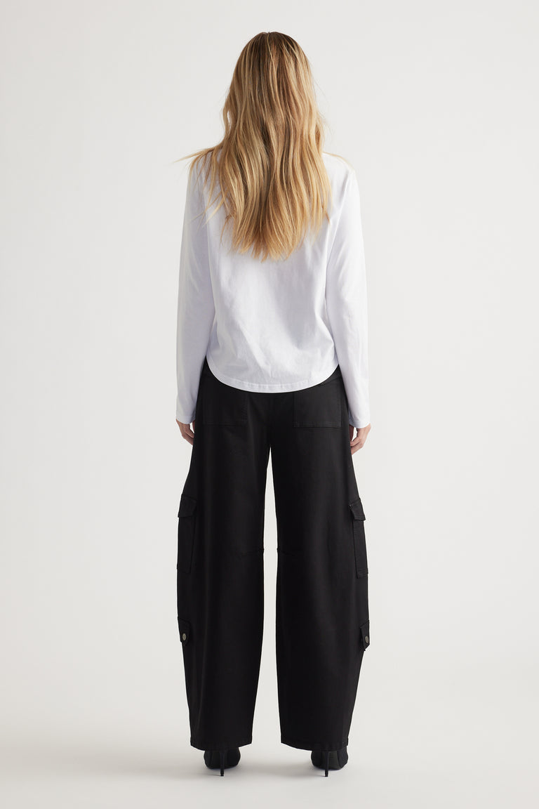 Woman seen from behind wearing a white long sleeve top paired with loose black wide-leg pants with pockets.