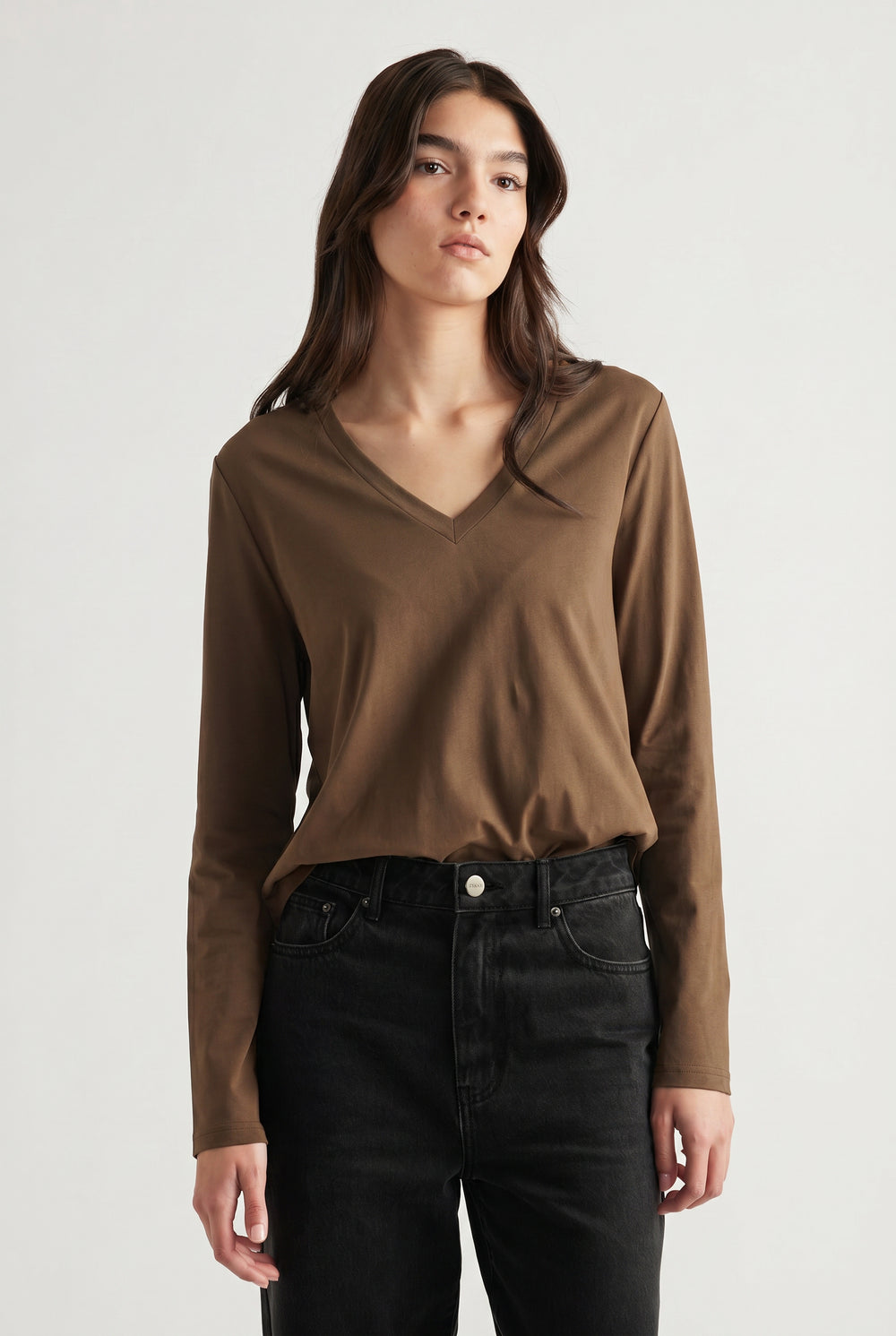 Woman wearing a brown V-neck long sleeve top paired with high-waisted black jeans for a casual look