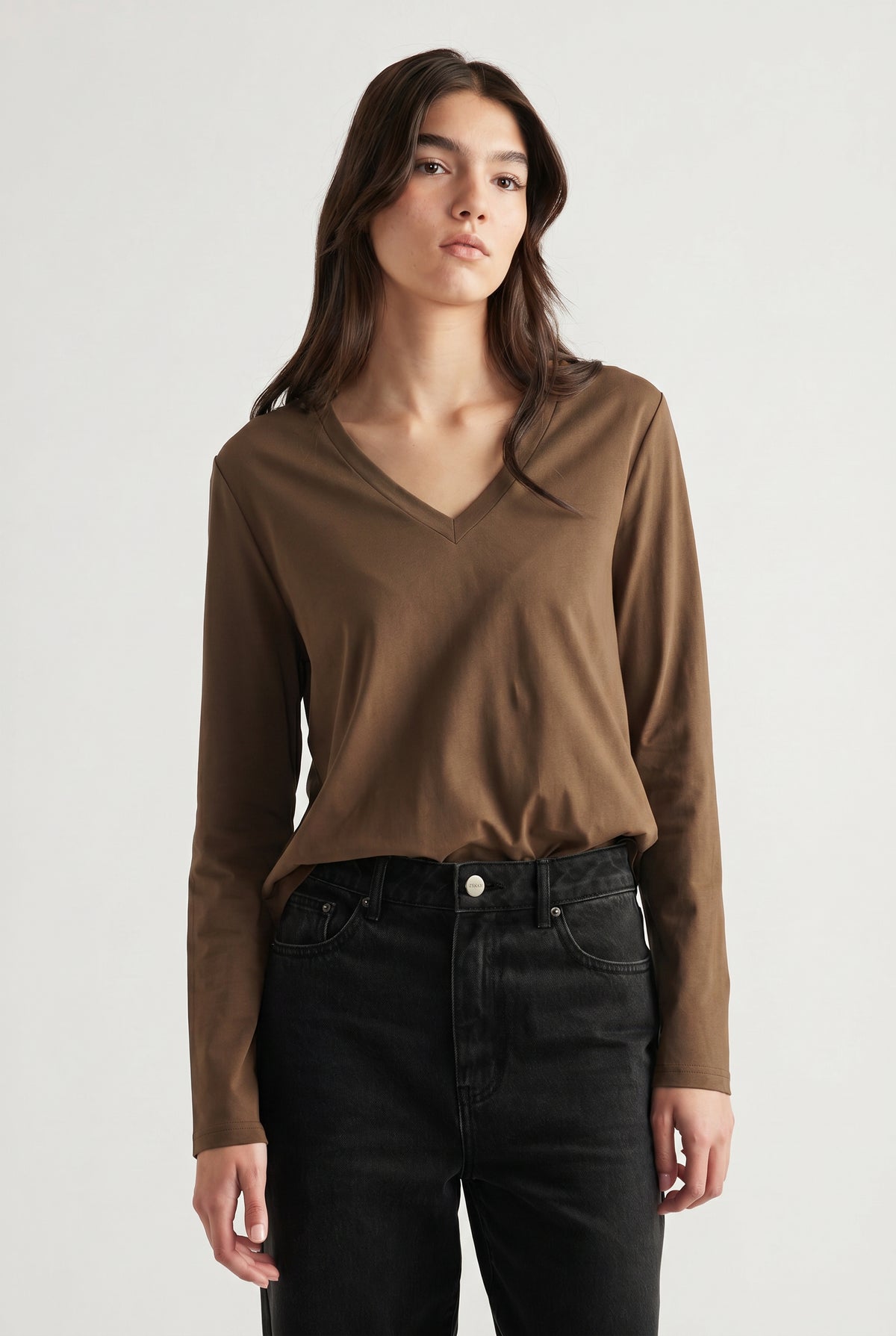 Woman wearing a brown V-neck long sleeve top paired with high-waisted black jeans for a casual look