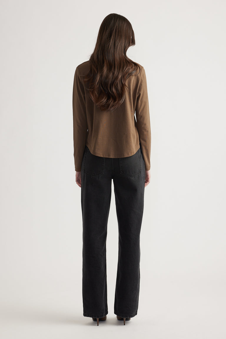 Woman with long hair wearing a fitted brown long sleeve top paired with relaxed black straight-leg jeans and heels