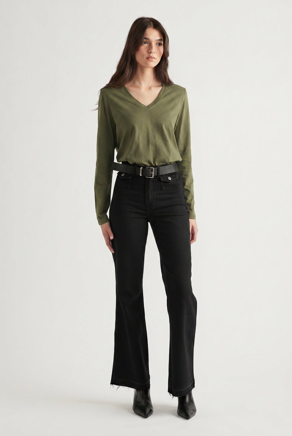 Woman wearing an olive V-neck long sleeve top tucked into high-waisted black flared jeans with a belt and boots
