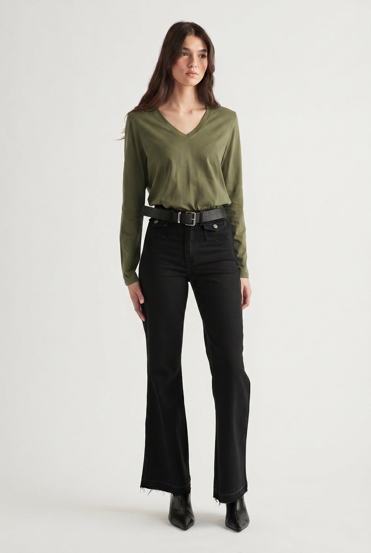 Woman wearing an olive V-neck long sleeve top tucked into high-waisted black flared jeans with a belt and boots