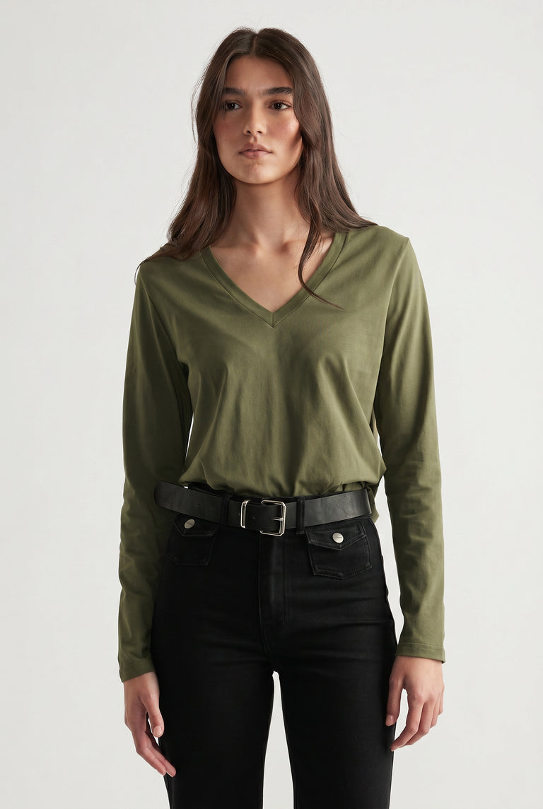 Woman wearing an olive green V-neck long sleeve top tucked into high-waisted black jeans with a black belt.