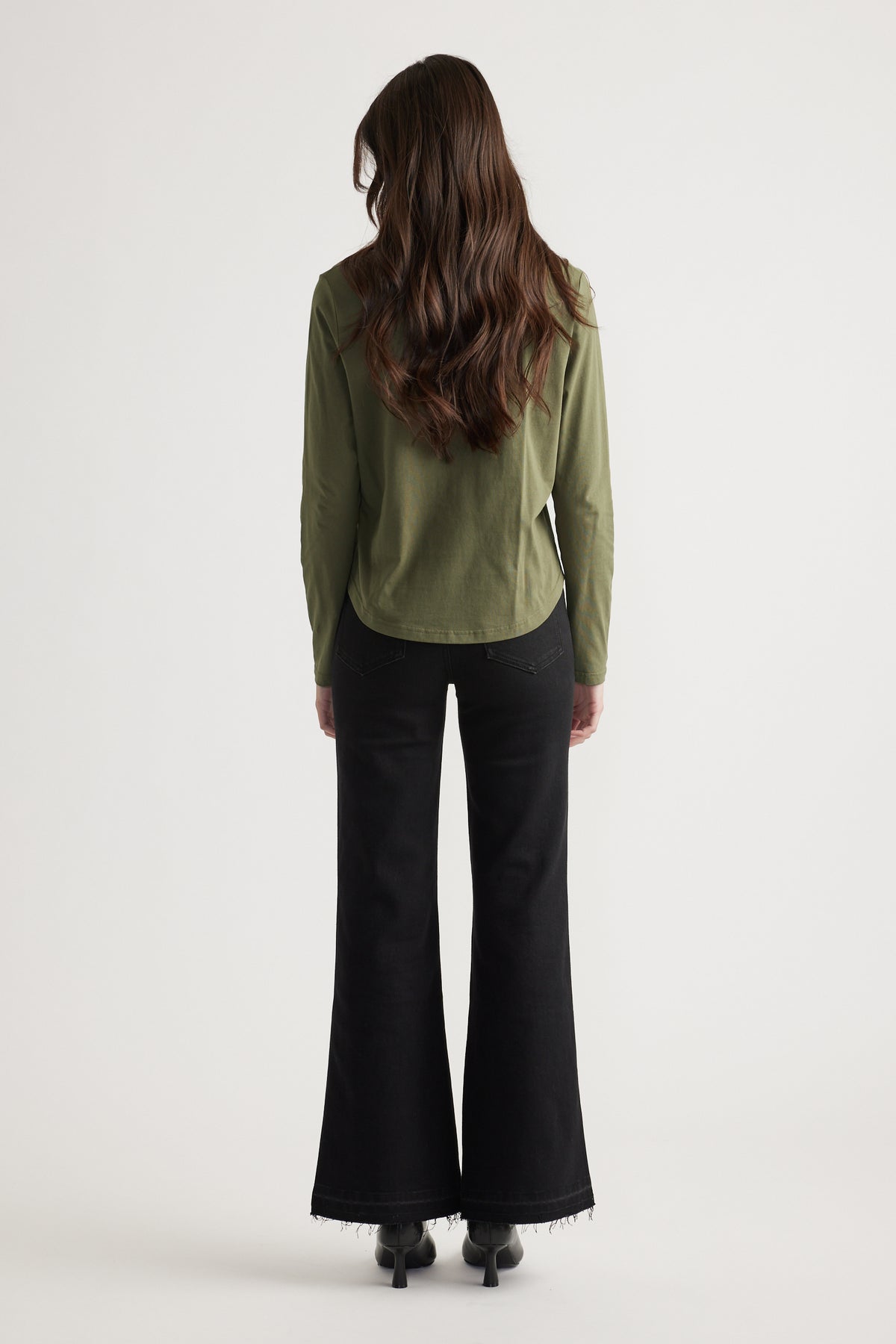 Back view of woman wearing an olive long-sleeve top paired with high-waisted black flared jeans and boots