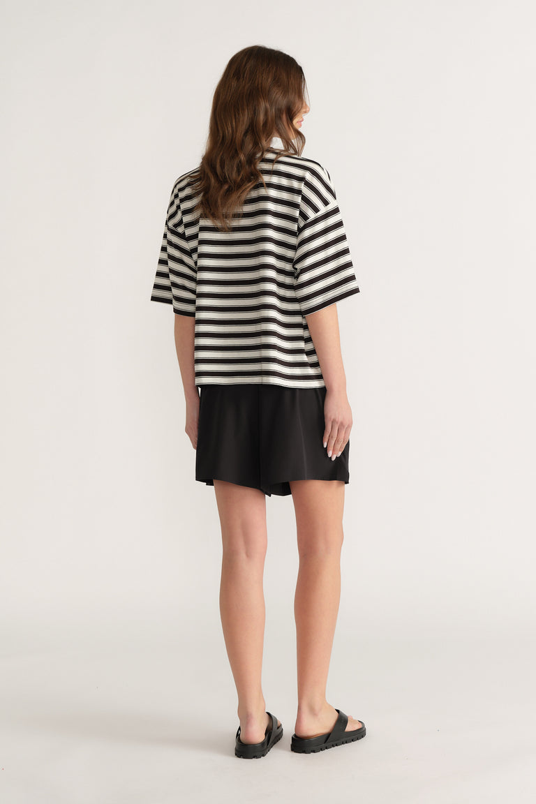 Woman seen from behind in an oversized black and white striped tee with black shorts and sandals