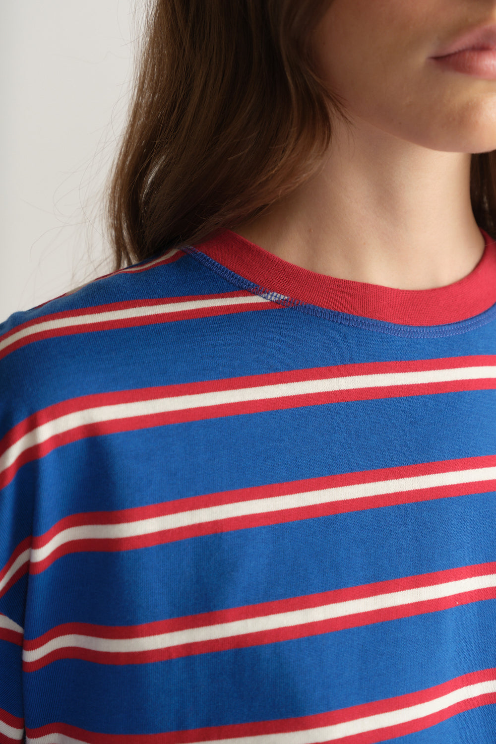 Close up of a woman wearing a blue oversized tee with red and white stripes and a contrasting red crew neckline
