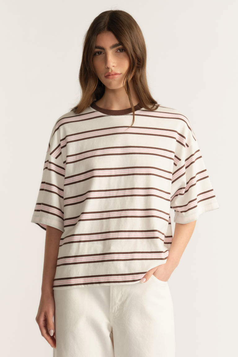 Woman wearing an oversized cream and brown striped tee with white pants