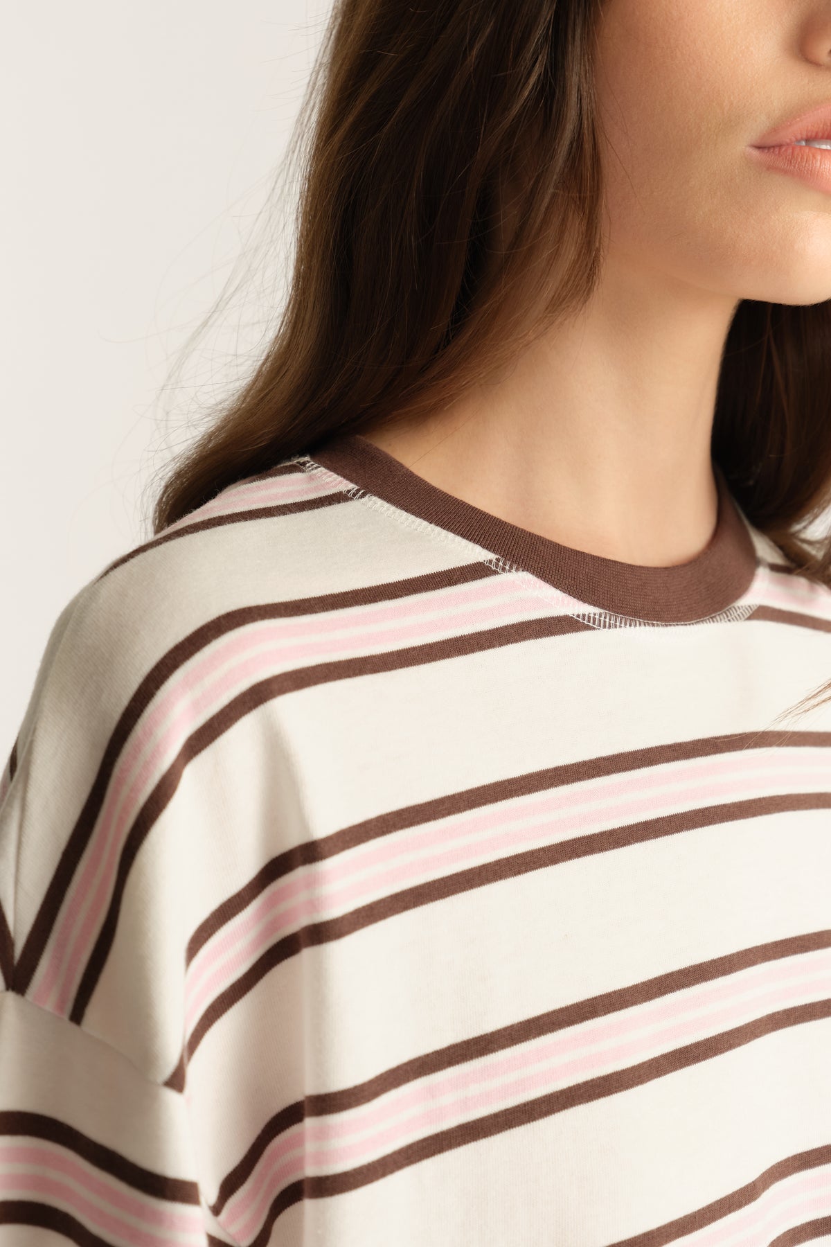 Close-up of a woman wearing an oversized cream tee with pink and brown stripes and a contrast crew neck