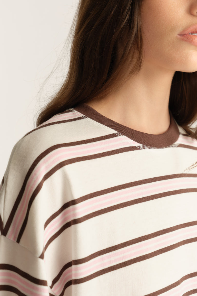 Close-up of a woman wearing an oversized cream tee with pink and brown stripes and a contrast crew neck