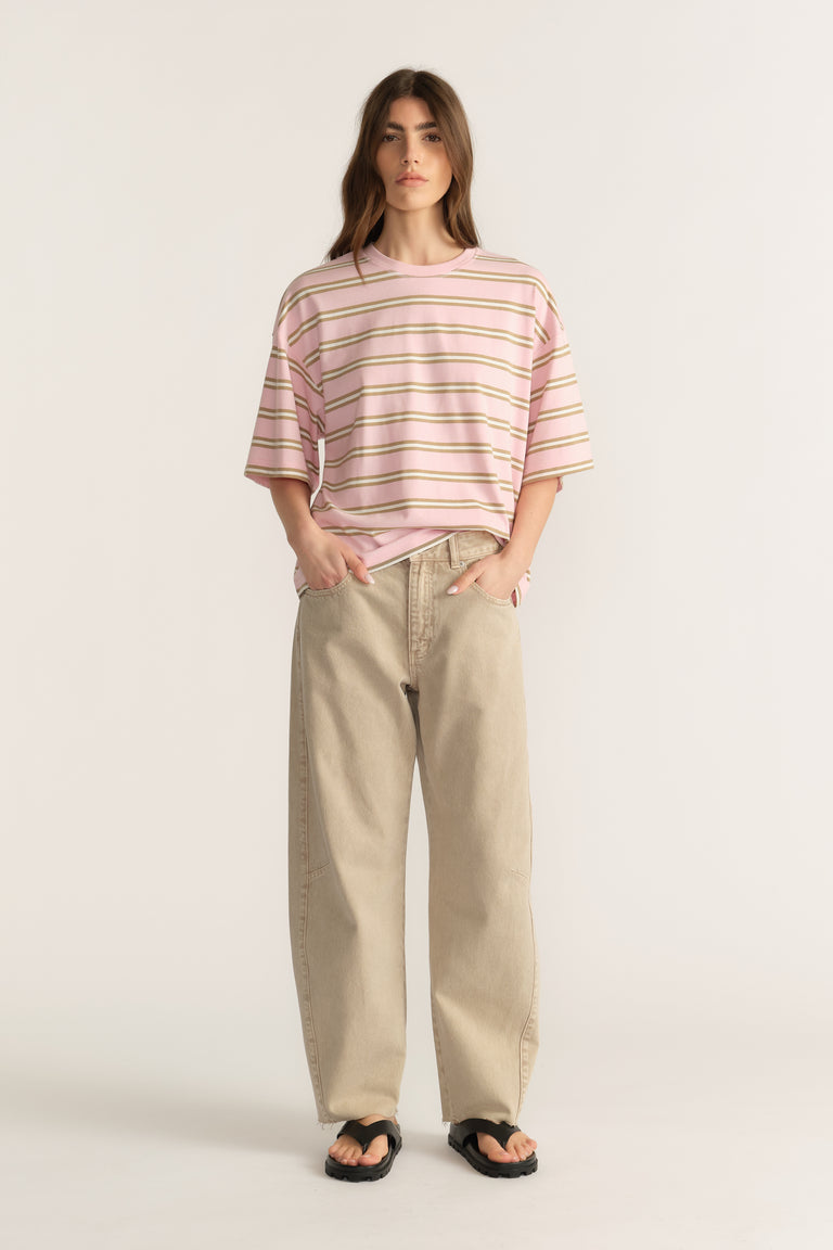 Woman wearing an oversized pink and green striped tee with beige wide leg jeans and black sandals