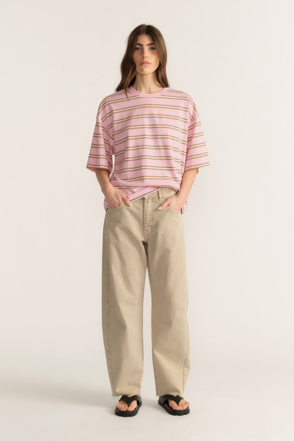 Woman wearing an oversized pink striped crew neck tee with beige wide leg pants and sandals
