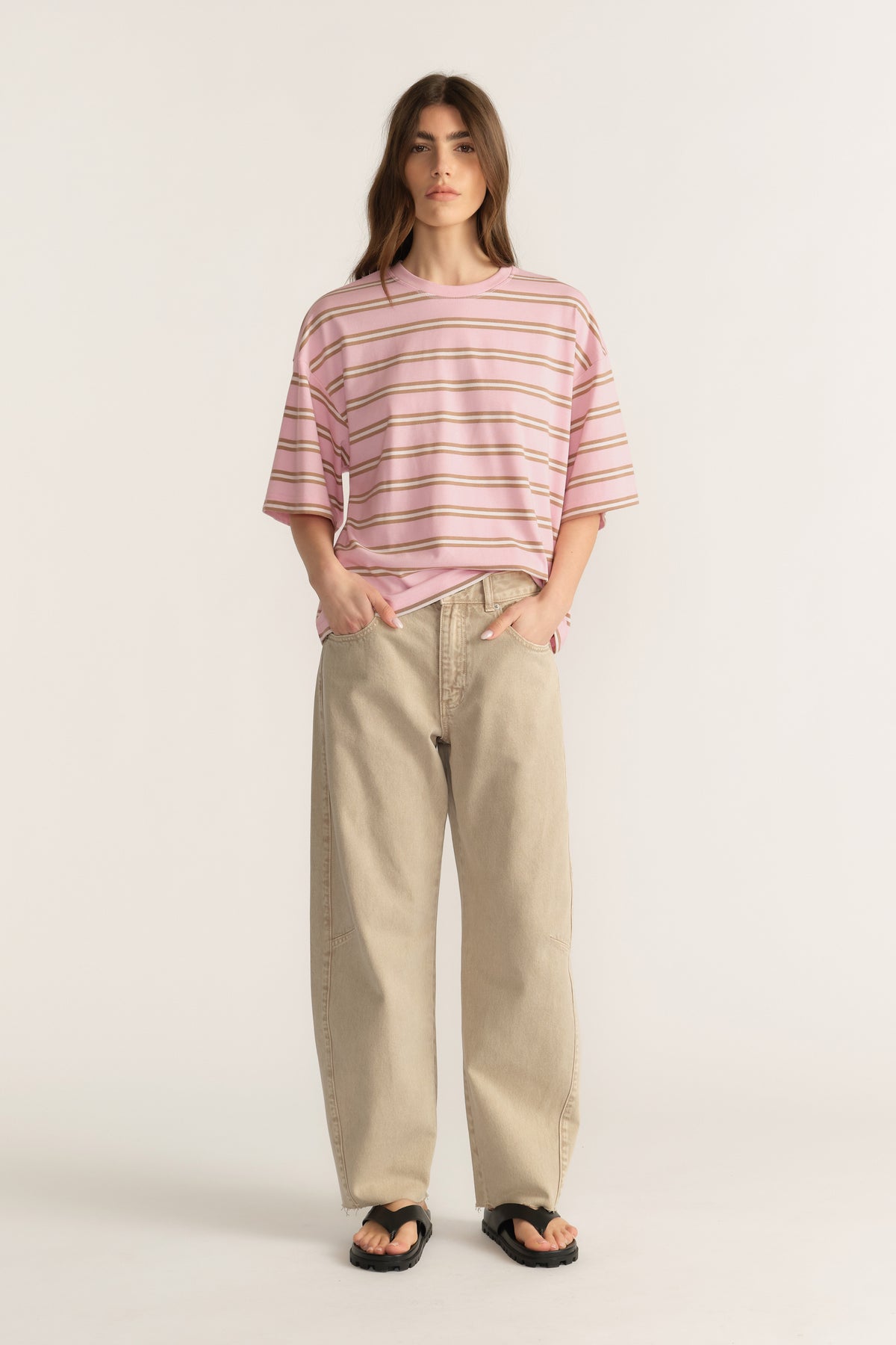 Woman wearing an oversized pink striped crew neck tee with beige wide leg pants and sandals