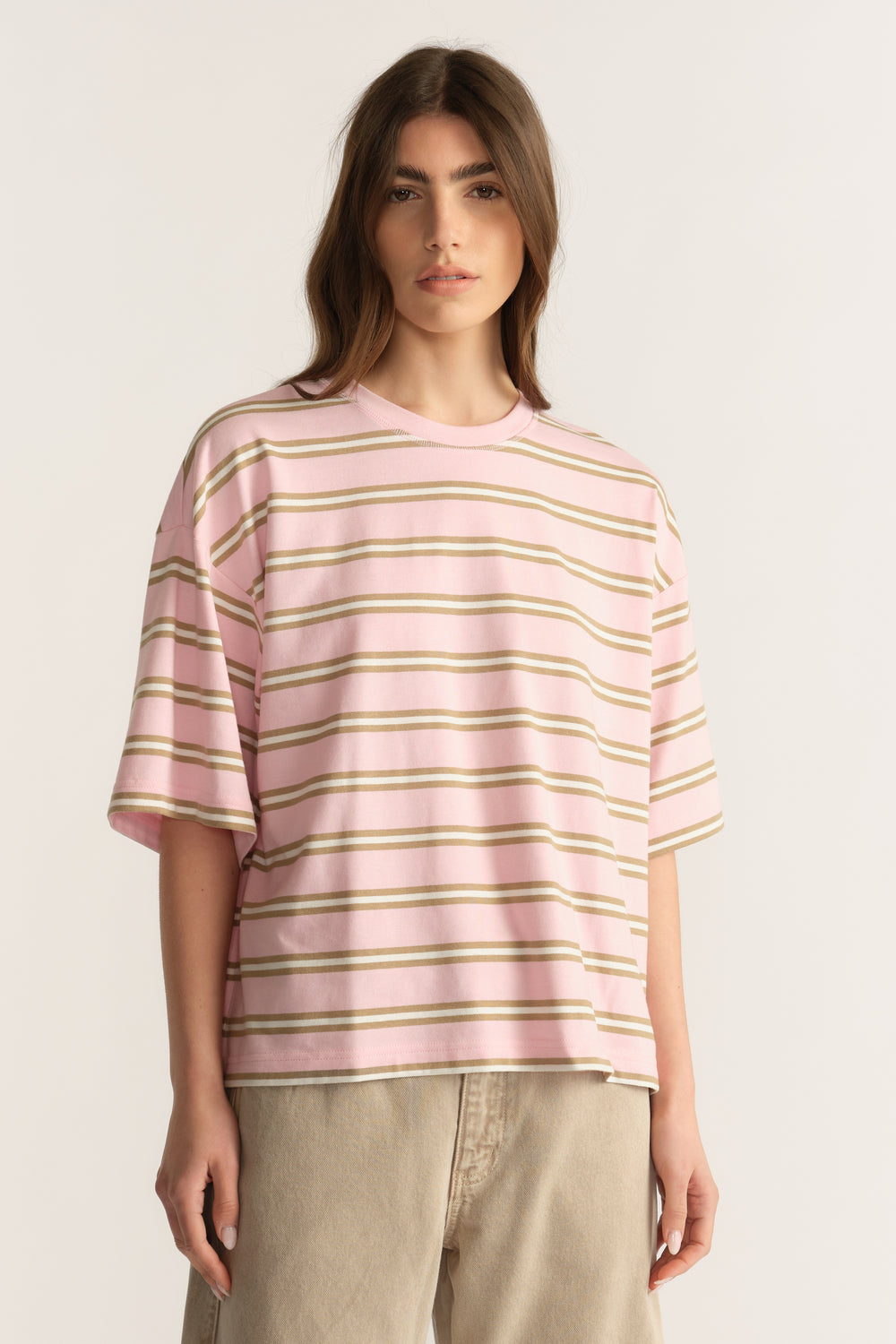 Woman wearing an oversized pink and beige striped tee with beige pants