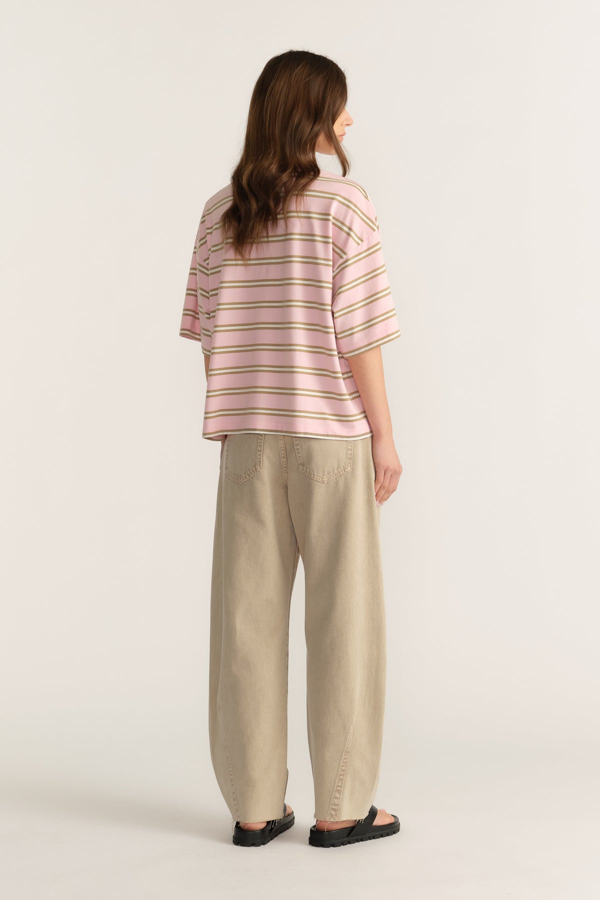Woman wearing a pink striped oversized tee with beige pants and black sandals