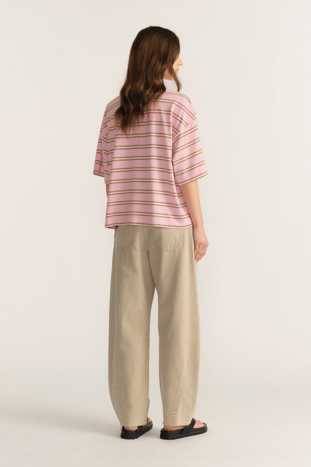 Woman wearing an oversized pink striped tee with beige pants and black sandals, viewed from behind