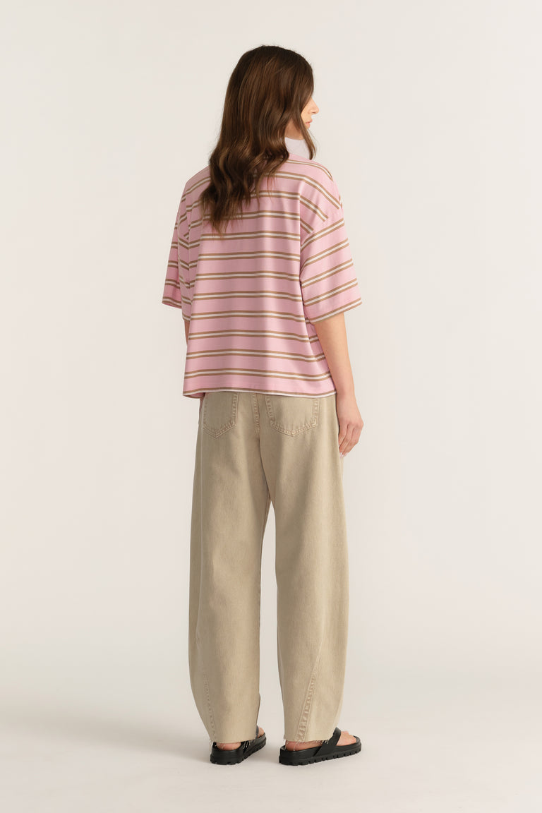 Woman wearing an oversized pink striped tee with beige pants and black sandals, viewed from behind