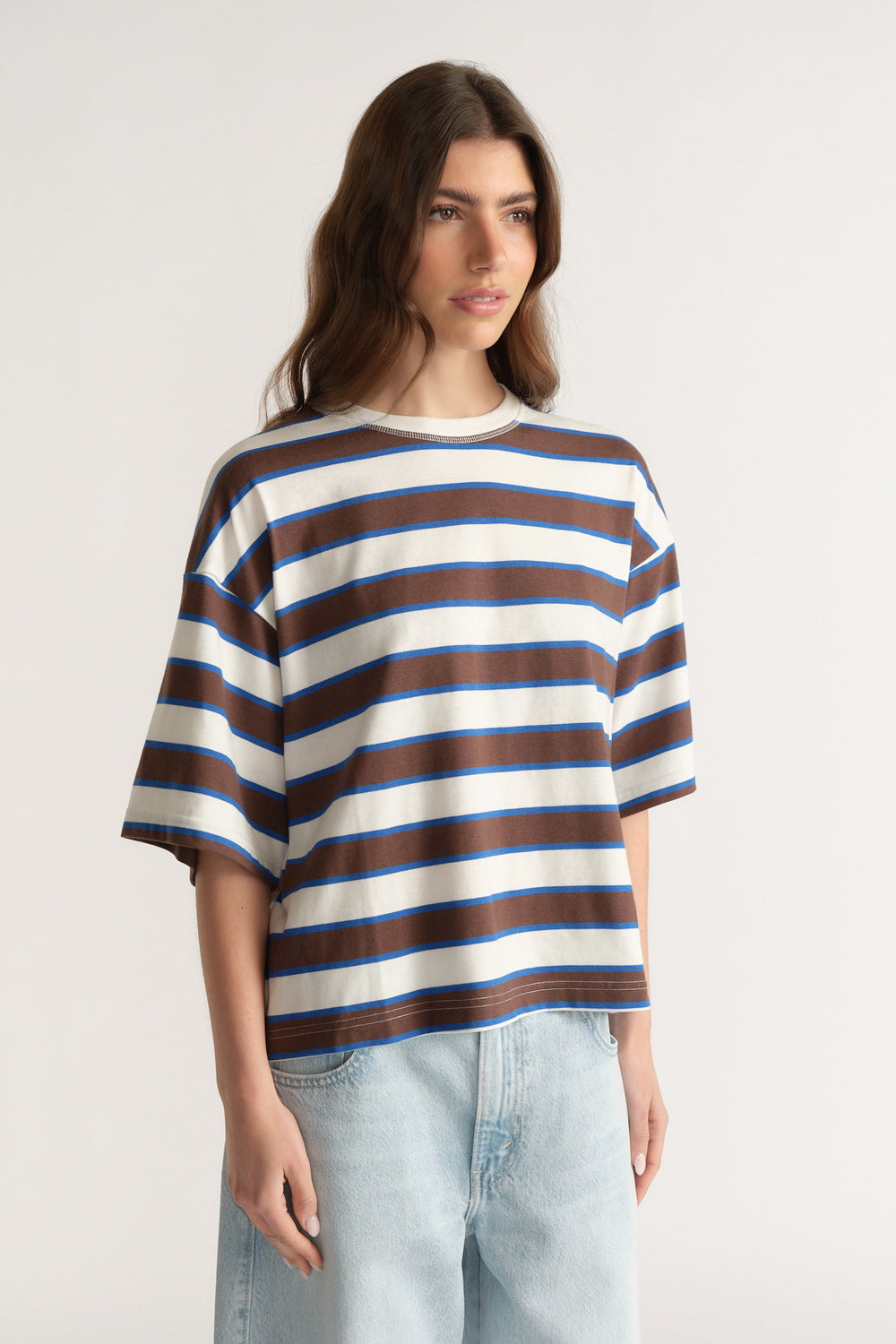 Woman wearing an oversized blue, brown and white striped tee with light wash jeans