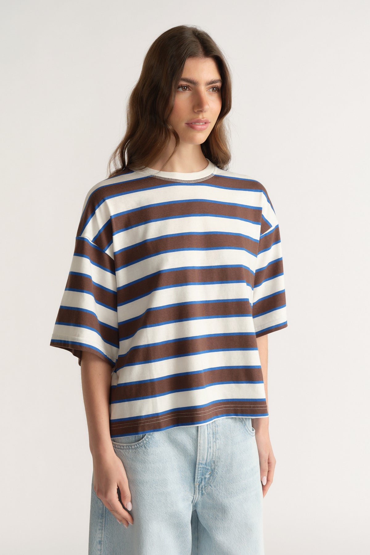 Woman wearing an oversized blue, brown and white striped tee with light wash jeans
