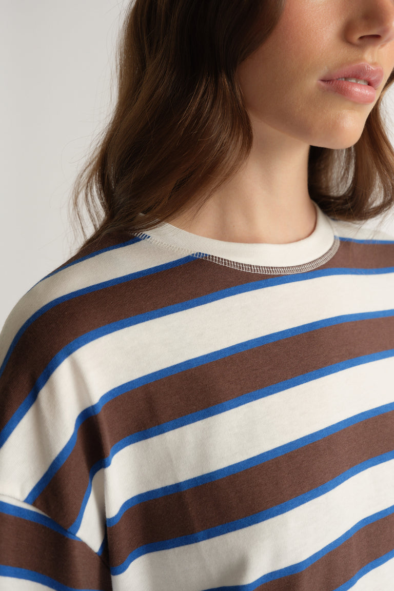 Woman wearing an oversized cream tee with brown and blue horizontal stripes