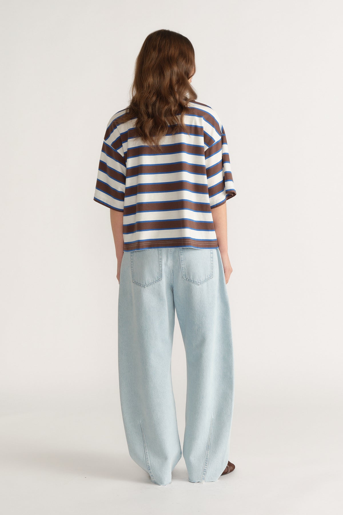 Back view of a woman wearing an oversized blue and white striped tee with light wide leg jeans