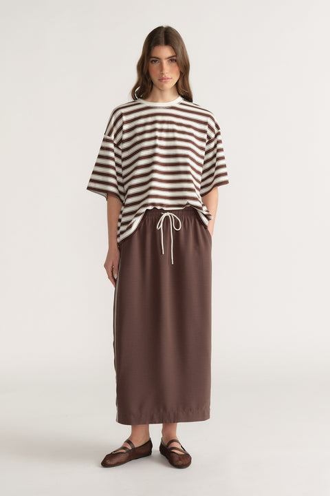 Woman wearing an oversized brown and white striped tee with a brown drawstring midi skirt and sandals
