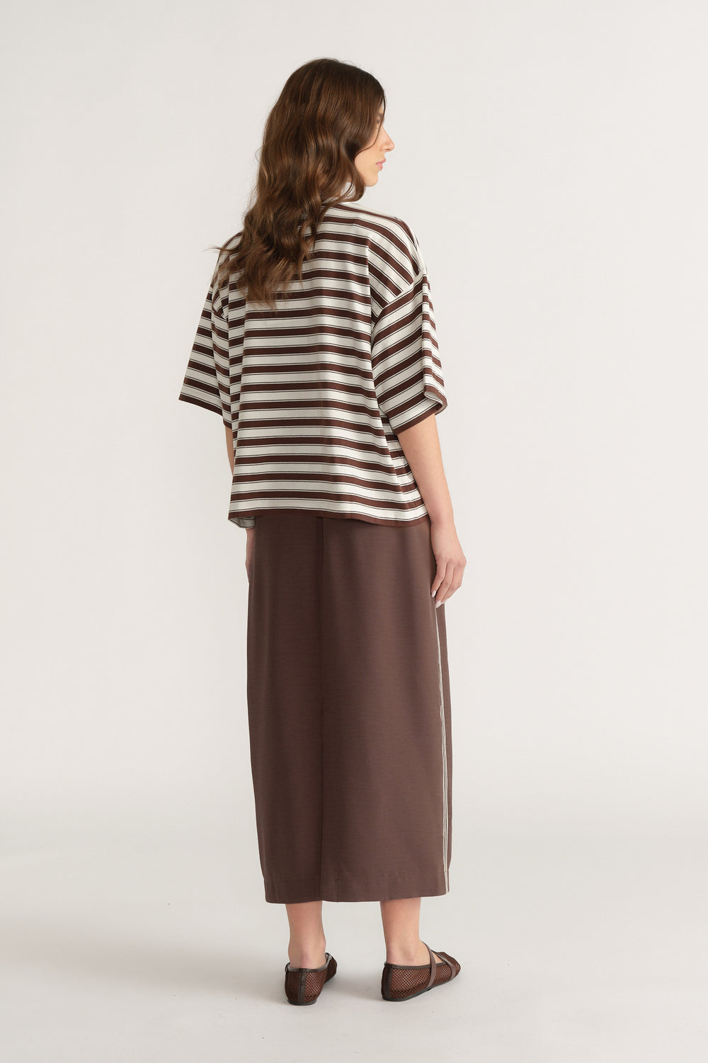Back view of a woman wearing an oversized brown and white striped tee with a brown midi skirt