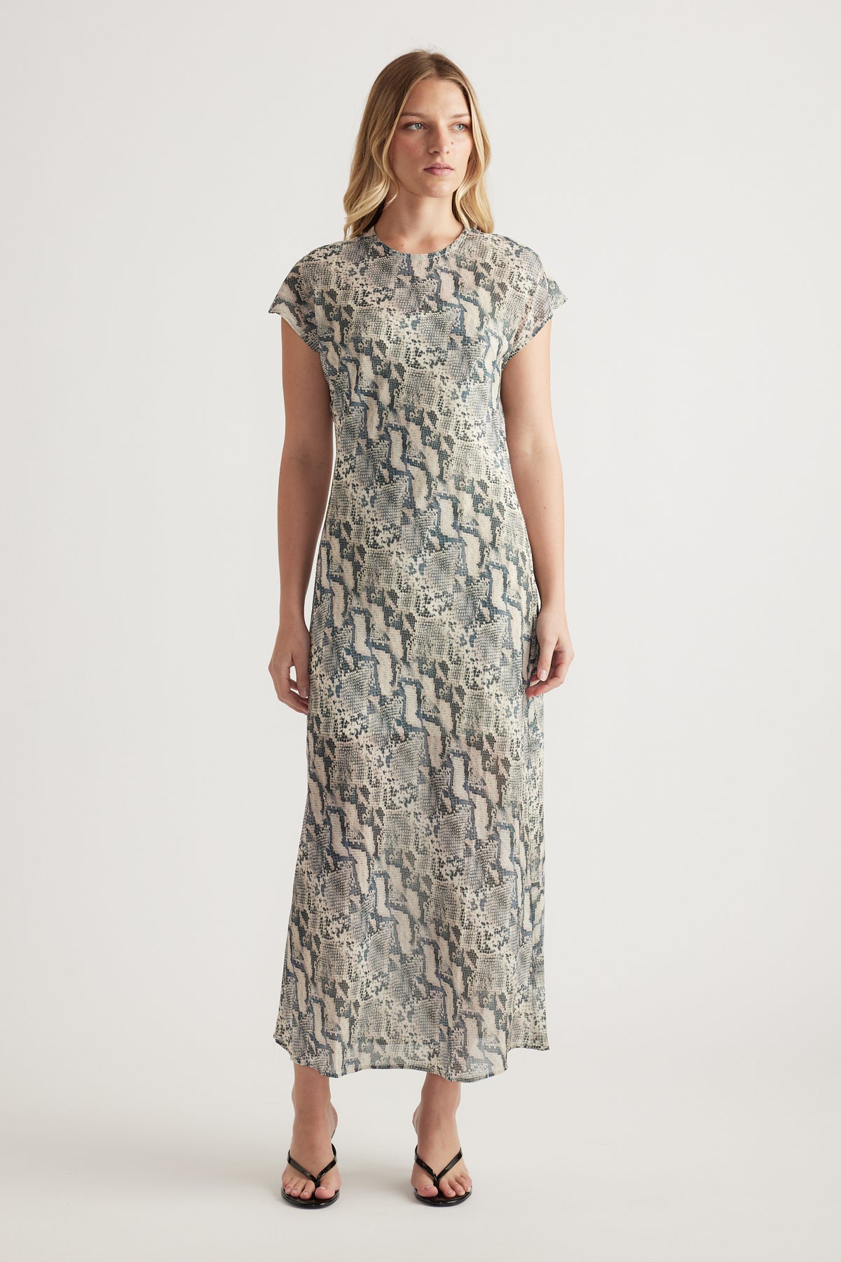 Woman wearing a grey snake print midi dress with short sleeves and black thong sandals