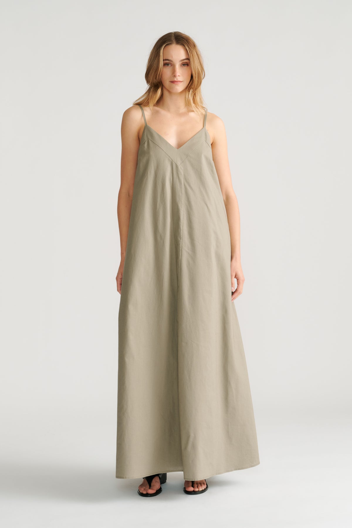 Woman wearing a relaxed fit sage green maxi dress with thin straps and a V-neckline paired with black sandals.