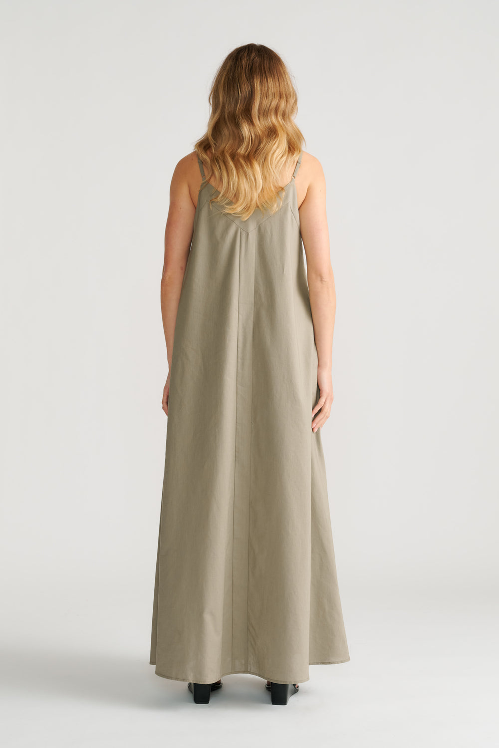 Woman wearing a sage green trapeze maxi dress with thin straps and a relaxed, flowing silhouette, back view.