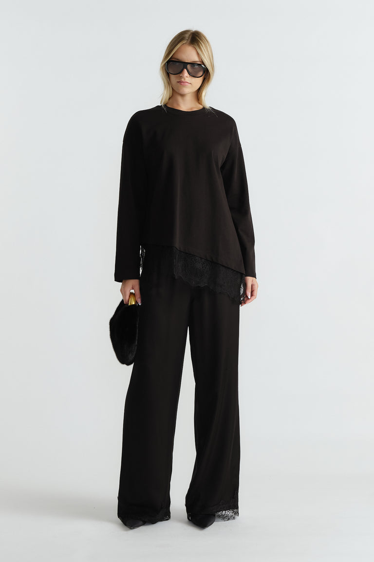 Woman wearing a black long sleeve top with lace trim and matching wide-leg pants, carrying a black fur clutch.