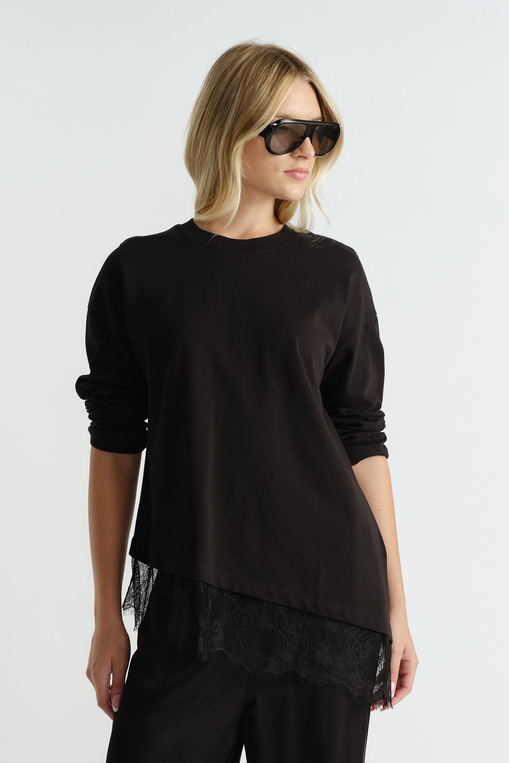 Black long sleeve top with asymmetrical lace hem detail, styled with casual black pants and oversized sunglasses.