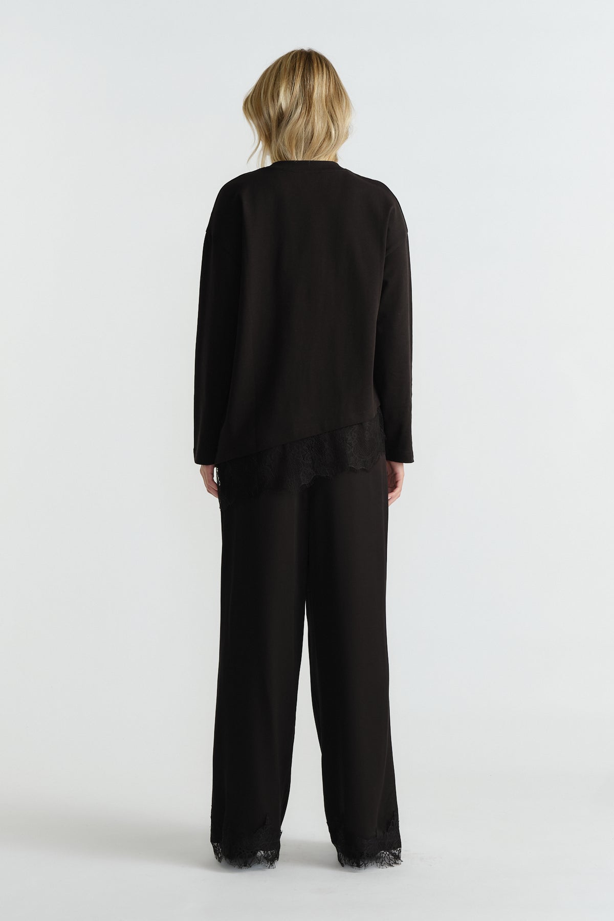 Woman wearing a relaxed-fit black long sleeve top with lace trim and matching wide-leg pants with lace detail at the hem